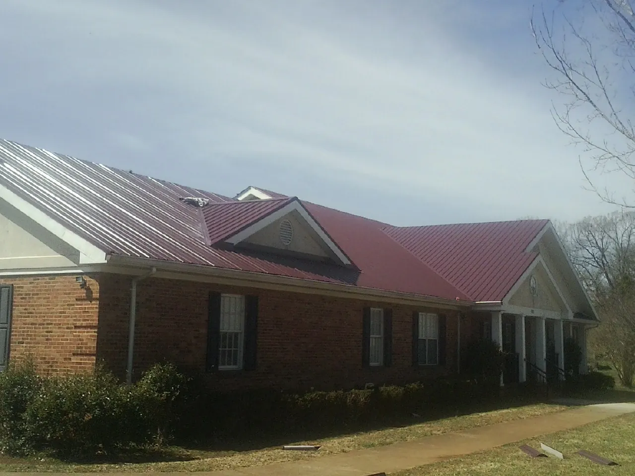 Red metal roof with gabled entries on a long brick building, from a Hail Damage Roof Repair job in Temple