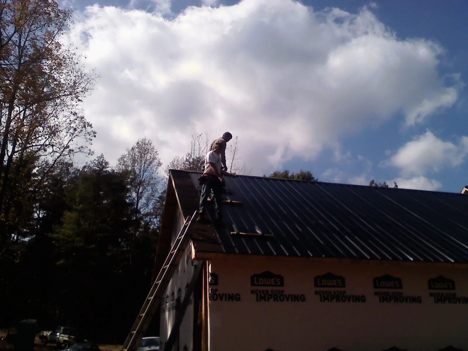 Roofer fastening dark metal panels high against a cloudy sky, from a Roof Inspection job in Temple